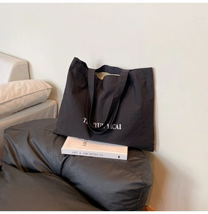 Detailed macro view of black nylon tote bag featuring white letter printing and fabric texture