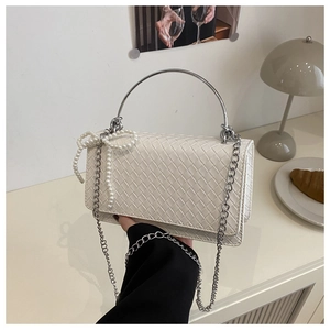 Detail of white woven shoulder bag featuring round silver handle and pearl bow charm