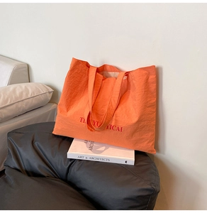 Detail of bright orange nylon tote bag with red lettering on a black leather chair