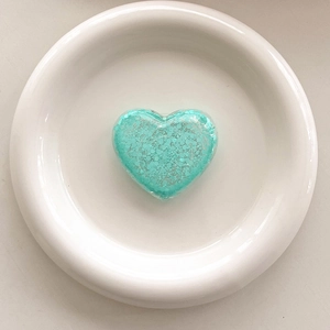 Macro detail of heart-shaped glitter phone grip in mint green on white ceramic plate