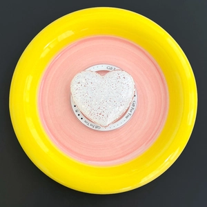 Top view of white heart-shaped matte phone grip on a pink and yellow ceramic stand
