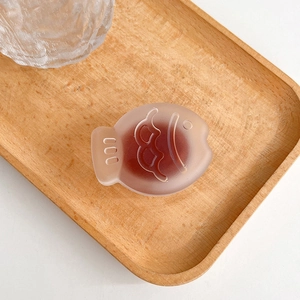 Detail of a frosted translucent red-brown fish-shaped phone grip on a wooden tray