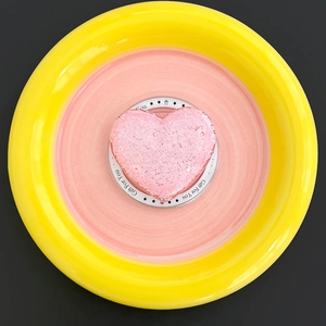 Macro detail of a heart-shaped pink bath bomb with crystal texture and a gift card