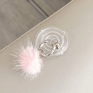 Close-up of a soft pink faux fur pompom phone holder with a silver ring on a leather surface