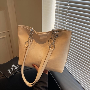 Minimalist beige woven tote bag with silver chain straps shown in an aesthetic setting
