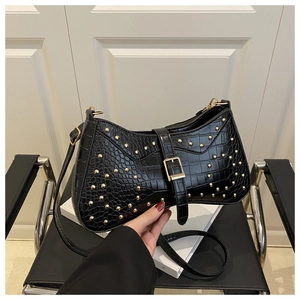 Detail view of black crocodile pattern leather bag with golden rivets and adjustable strap