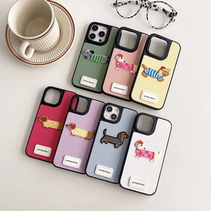 Custodia iPhone in pelle con ricamo bassotto 3D ed etichetta goodluck su scrivania bianca