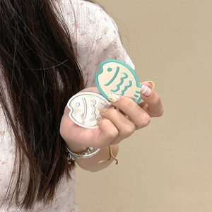 Close-up of fish-shaped phone grip mirrors in mint green and cream on floral dress