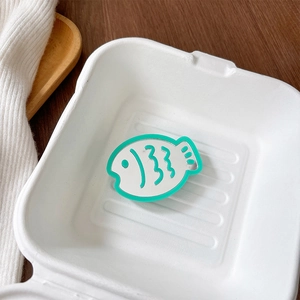 Close-up of mint green fish-shaped phone grip mirror inside a white paper takeout box