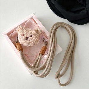 Detail of plush bear charm on beige woven crossbody strap with metal hooks in gift box
