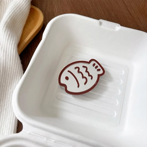 Close-up of cute fish-shaped phone grip mirror with white enamel finish on wooden tray