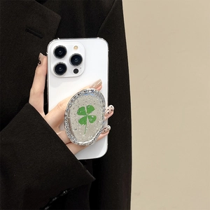Close-up of a silver foil clover phone grip on a white smartphone held by a model