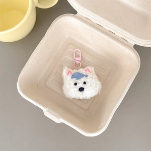 Close-up of white plush puppy pendant with blue cap and pink hook in a rustic tray
