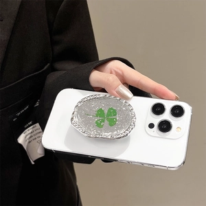 Detailed view of oval metal phone grip with green four-leaf clover and silver texture
