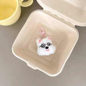 Close-up of white plush puppy charm with black glasses and pink clasp in a beige tray