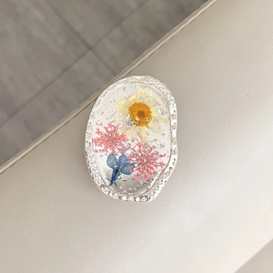 Macro detail of oval phone stand with real dried flowers and silver foil in resin