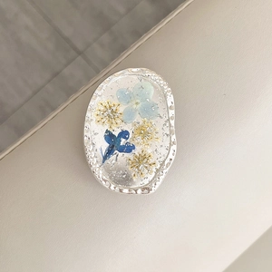 Macro shot of oval resin phone grip featuring blue dried flowers and silver foil flakes