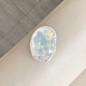 Detail of oval metal phone grip with silver foil and real blue dried flowers inside