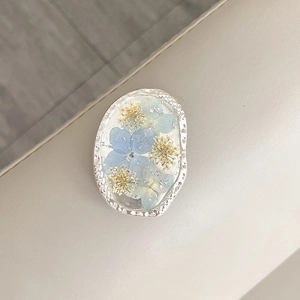 Close-up of silver metal phone grip with blue dried flowers and silver foil flakes