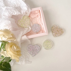 Sparkly heart and round resin phone grips with iridescent glitter on a pink floral background