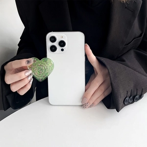Close-up of green glitter heart phone grip stand on a white case held by model