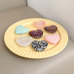Detailed top view of 7 colorful glitter heart-shaped expanding phone grips on a ceramic plate