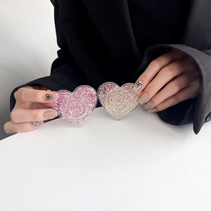 Detail of heart-shaped glitter phone grips in pink and gold held by hand
