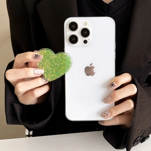 Close-up of heart-shaped green glitter phone socket grip held against a white smartphone