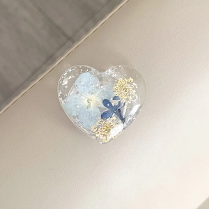 Macro detail of heart-shaped resin phone grip with blue dried flowers and silver foil