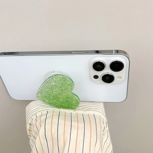 Detail of a green heart-shaped glitter phone socket holder attached to a white smartphone
