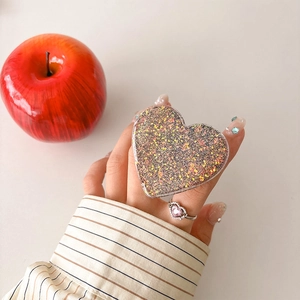 Detail of a heart-shaped phone grip with glitter sequins held against a warm background