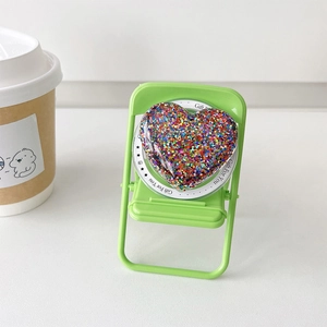 Detail of heart-shaped glitter MagSafe phone grip on a mini chair display with coffee cup
