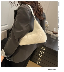 Close-up of cream shoulder bag with triangle texture and metal bottom studs on gray suit
