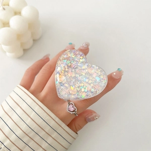 Close-up of heart-shaped glitter phone grip and matching pink gemstone ring on hand