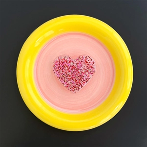 Macro detail of heart-shaped phone grip filled with pink and red sequins on a plate