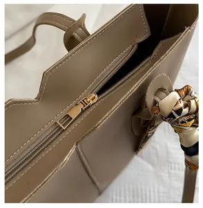 Close-up of smooth gold zipper detail and decorative printed silk scarf on brown tote bag