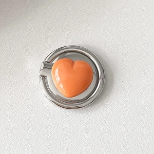 Detail view of the orange heart shaped mobile phone ring holder with silver metal finish