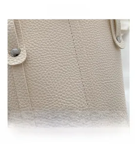 Macro shot of off-white lychee grain leather handbag with stitching and silver rivets