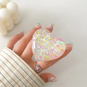 Detail of a transparent heart-shaped phone grip with iridescent glitter and star sequins