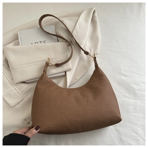 Détail d'un sac hobo tissé marron avec crochets dorés sur un blazer beige et draps