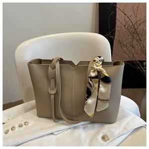 Close-up of beige tote bag with smooth texture and stylish silk scarf on the handle