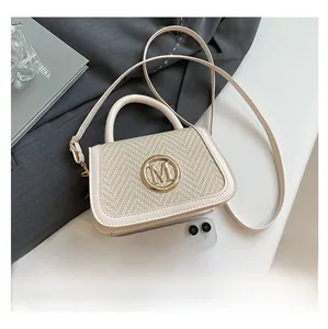Detail of beige straw handbag with leather trim and gold M logo next to a smartphone