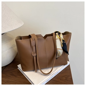 Detail of a brown vintage tote bag with contrast stitching and a patterned silk scarf handle