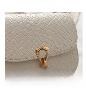 Close-up of white woven leather saddle bag with a vintage gold arch-shaped buckle lock