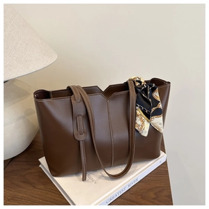 Close-up of brown tote bag with contrast stitching and silk scarf on a wooden table