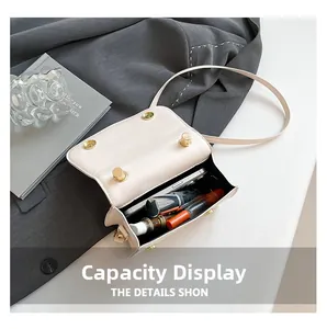 Detail view of the mini beige box bag interior holding a smartphone and lipsticks