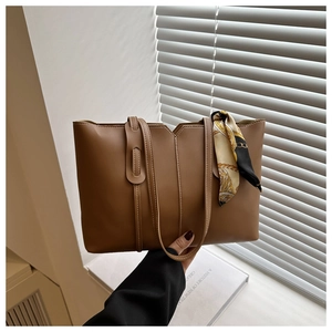 Detail of a brown leather tote bag with a decorative silk scarf held in an indoor setting