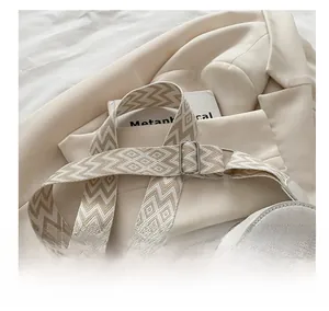 Detail of wide woven geometric shoulder strap and heart-shaped bag on a beige blazer
