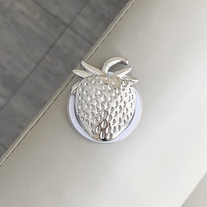 Detailed macro view of silver strawberry-shaped metal phone stand on beige leather surface
