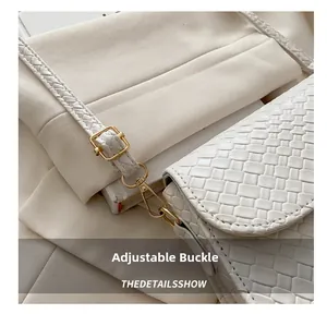 Detail of adjustable gold buckle and woven strap on a white leather shoulder bag
